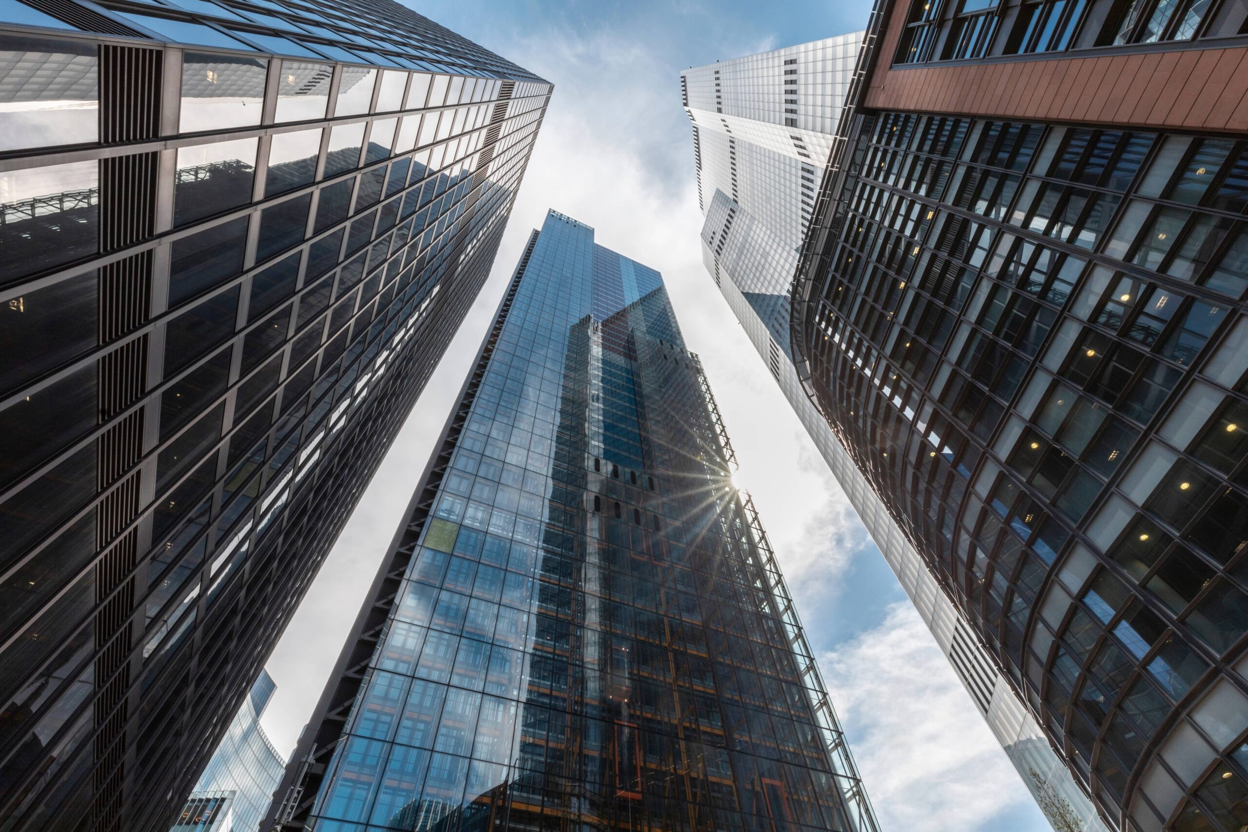 Tall skyscrapers with reflective glass facades viewed from below against a bright sky.